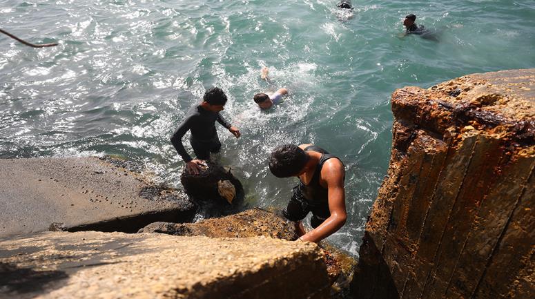 أطفال يمارسون السباحة قرب ميناء غزة المتضرر من الحرب، ويشكّل بحر غزة المتنفّس الوحيد للسكان الذين يعانون آثار الحرب والنزوح