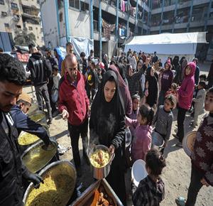 مواطنون يتجمعون لتلقي مساعدات غذائية من تكية خيرية في أحد مراكز الإيواء بمدينة غزة